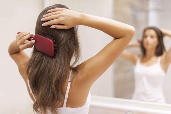 Frau pflegt schöne gesunde Haare vor Spiegel