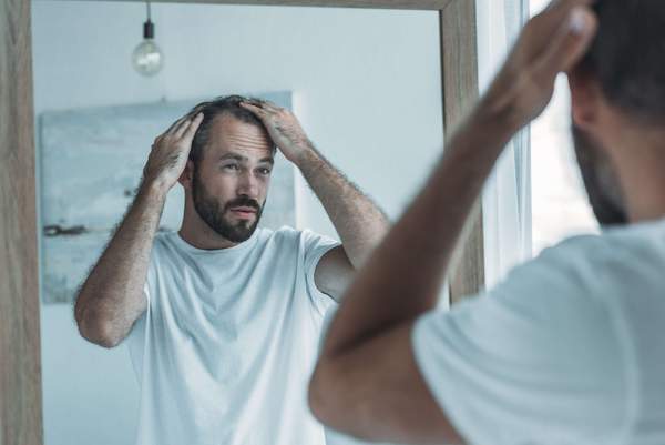Mann prüft Haarausfall im Spiegel